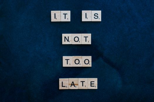 An inspiring message formed with wooden letter tiles on a dark surface: 'It is not too late'.