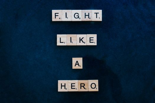 Scrabble tiles spelling 'Fight Like a Hero' on a textured blue background.