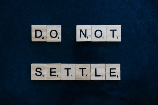 Wooden Scrabble tiles spelling 'Do Not Settle' on a dark surface, top view.
