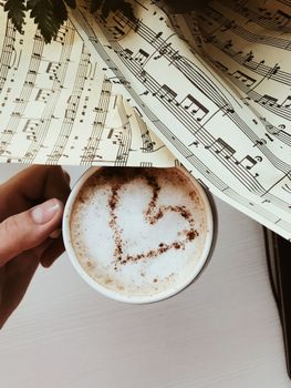 A cup of cappuccino with heart latte art on a background of musical notes.