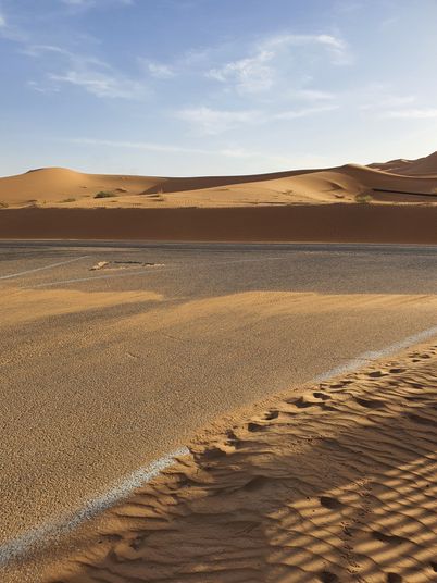 Sunlit sand dunes rolling toward a straight desert road, photo by Vjanodic WERSOV on Pexels