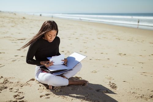 Free A young businesswoman sits on the beach, reviewing documents with focus and determination. Stock Photo