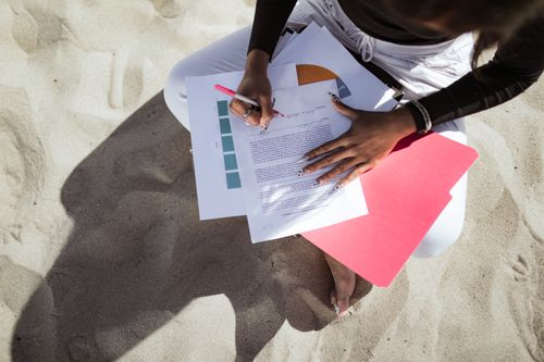 Free A person reviews and signs documents while sitting on a sandy beach, capturing a relaxed yet focused moment. Stock Photo