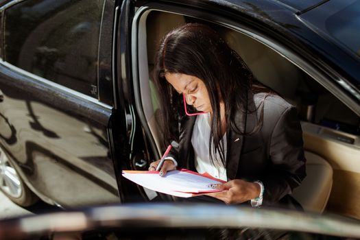 A focused businesswoman analyzes documents while sitting in her car.