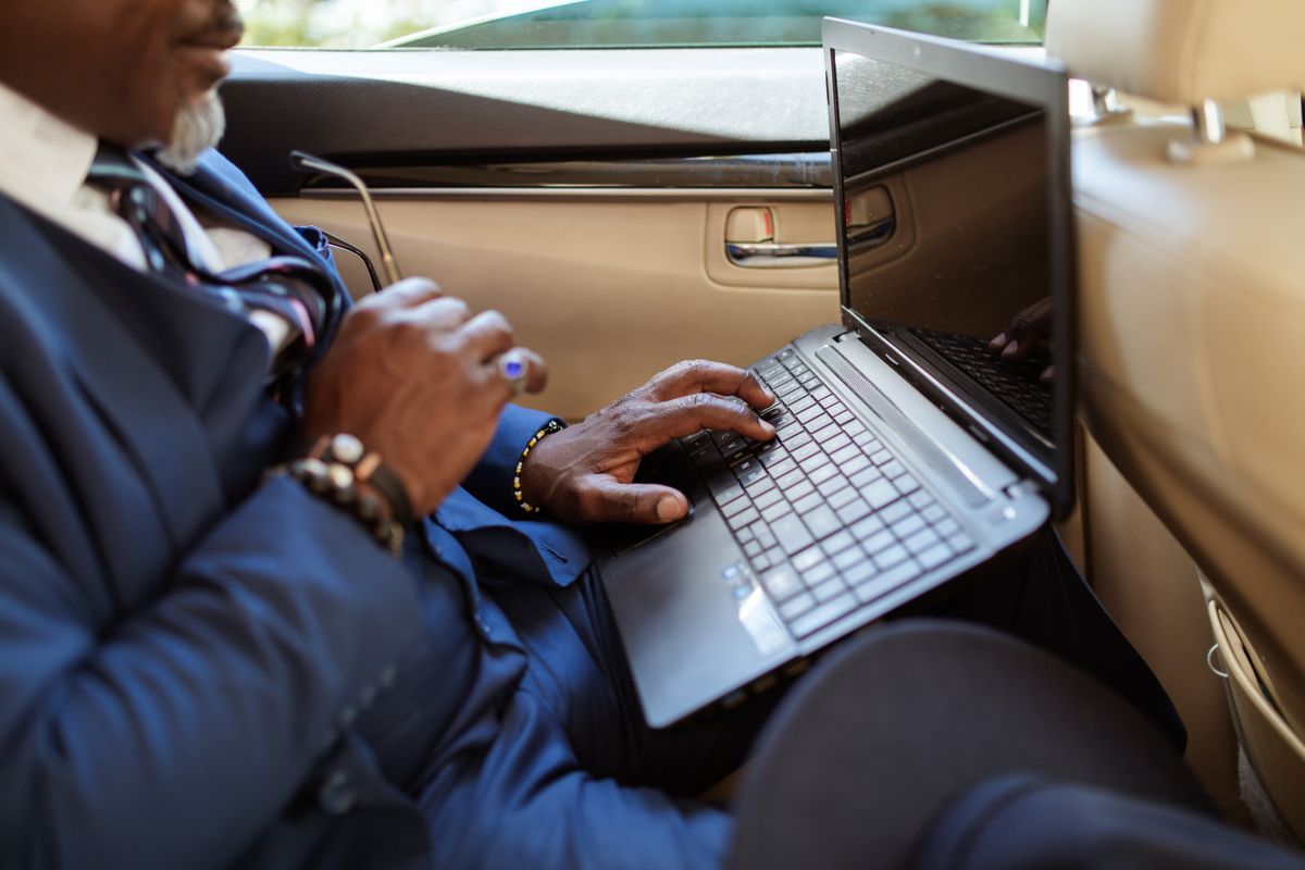 Client working on a laptop in the back of a chauffeured car