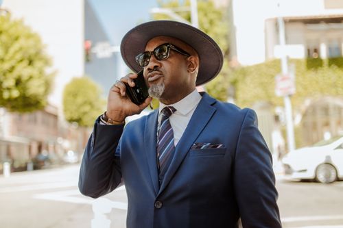 Free Confident man in a blue suit and hat having a phone conversation on a sunny city street. Stock Photo