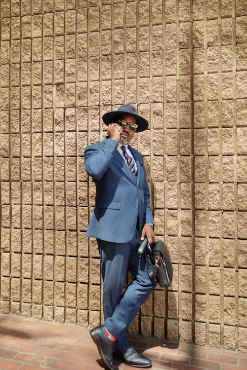 Free Dapper businessman in a blue suit talks on phone against a brick wall. Stock Photo