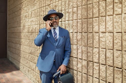 Free Fashionable man in a blue suit making a phone call while standing outdoors. Stock Photo