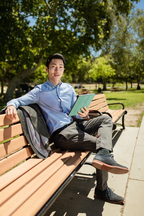 A Stylish Man Holding a Tablet while Sitting on a Park Bench