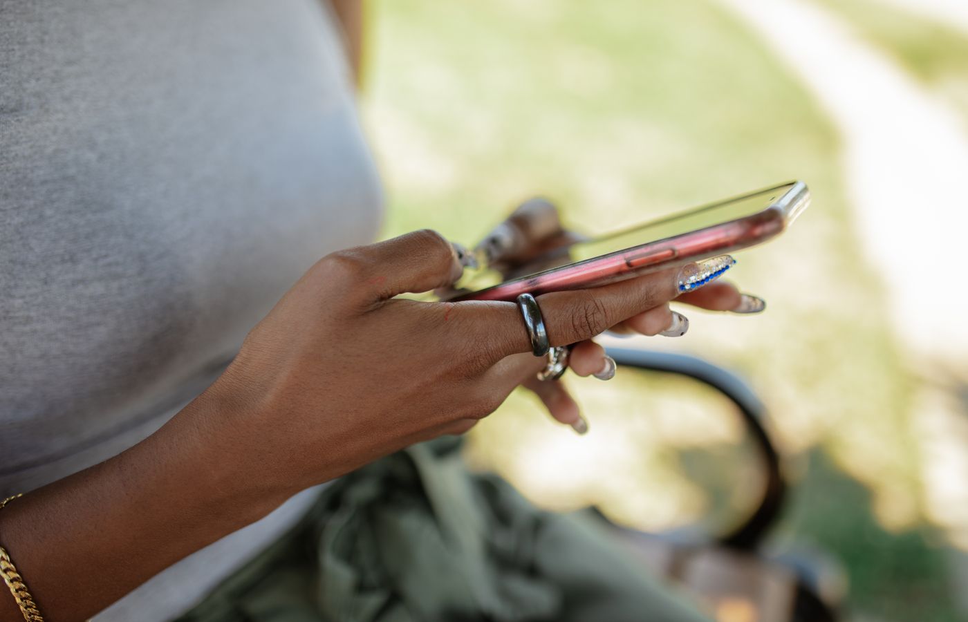Woman with acrylic nails holding smartphone while texting outdoors.