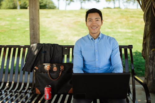 A Happy Man Using a Laptop while Sitting on a Park Bench