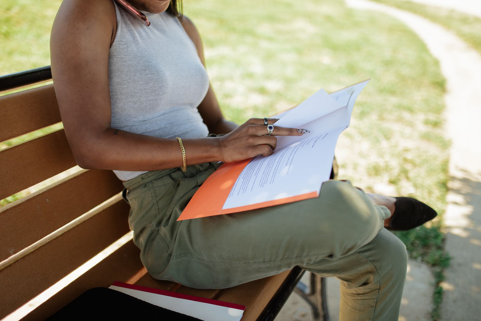 A woman sitting on a bench outdoors, reviewing documents on a sunny day.
