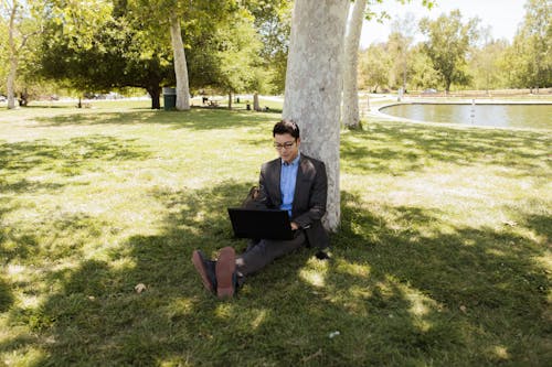 Free Man in Black Suit Sitting on Green Grass Working on His Laptop Stock Photo
