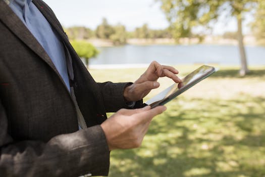 Businessman in suit using a tablet in a park setting near a lake.