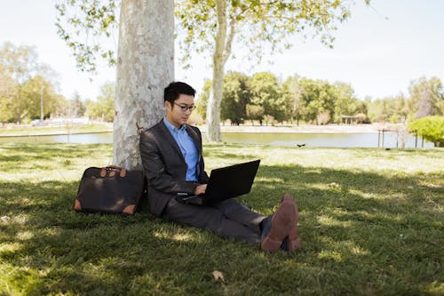 Free Man Sitting on Grass While Using a Laptop Stock Photo
