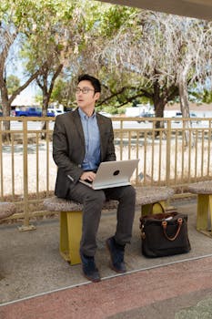 Asian businessman in corporate attire working on a laptop in a park.