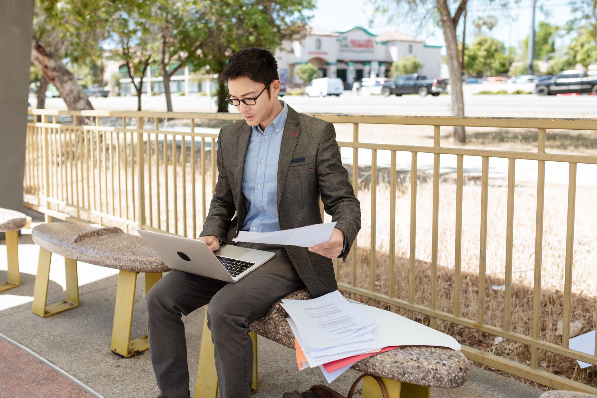 Young professional man working on a laptop outdoors, reviewing documents at a park.