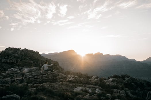 A hiker sitting on rocky terrain enjoys the sunrise over a mountain range.