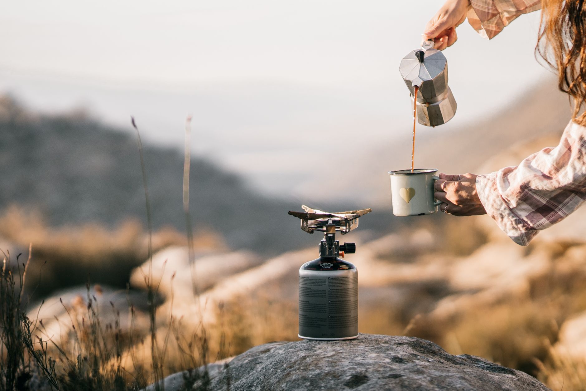 A serene scene of coffee being poured at a campsite, evoking morning tranquility.