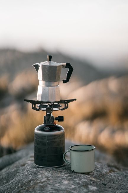 Compact backpacking stove boiling water beside a lightweight pot on a rocky campsite surface