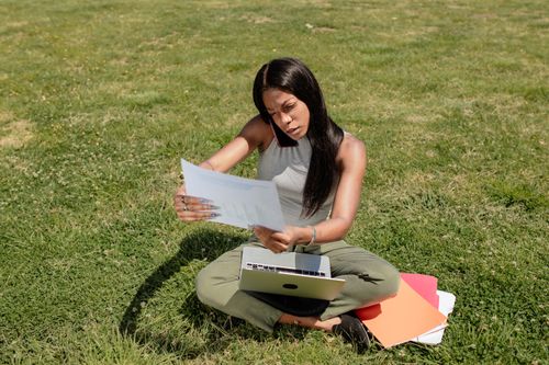 Free Businesswoman multitasking on phone and laptop outdoors, reviewing documents. Stock Photo