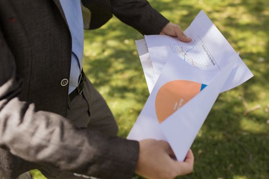 Man in suit holding financial reports in a sunny park.