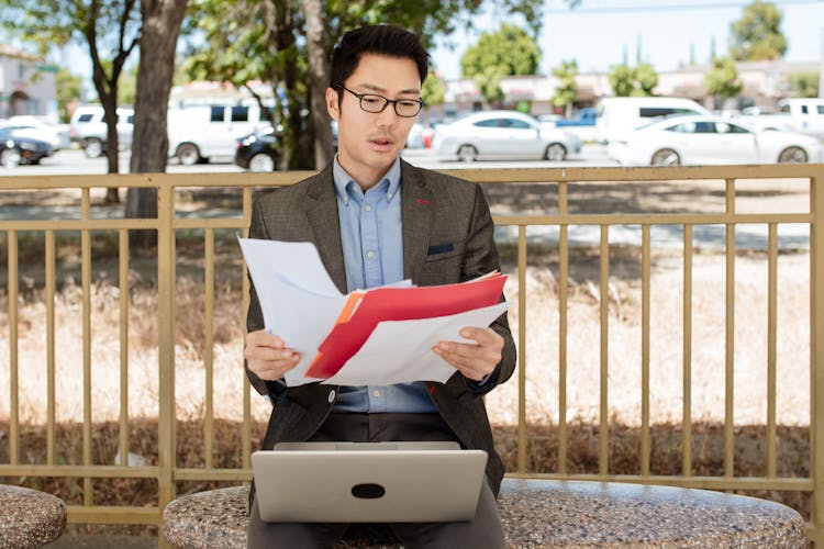 A Man In Black Suit Jacket And Black Pants Holding Paper Documents