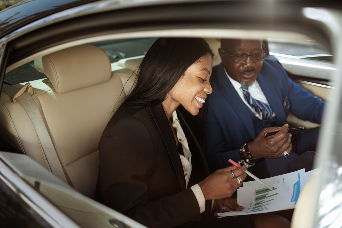 Two business professionals discussing work inside a car