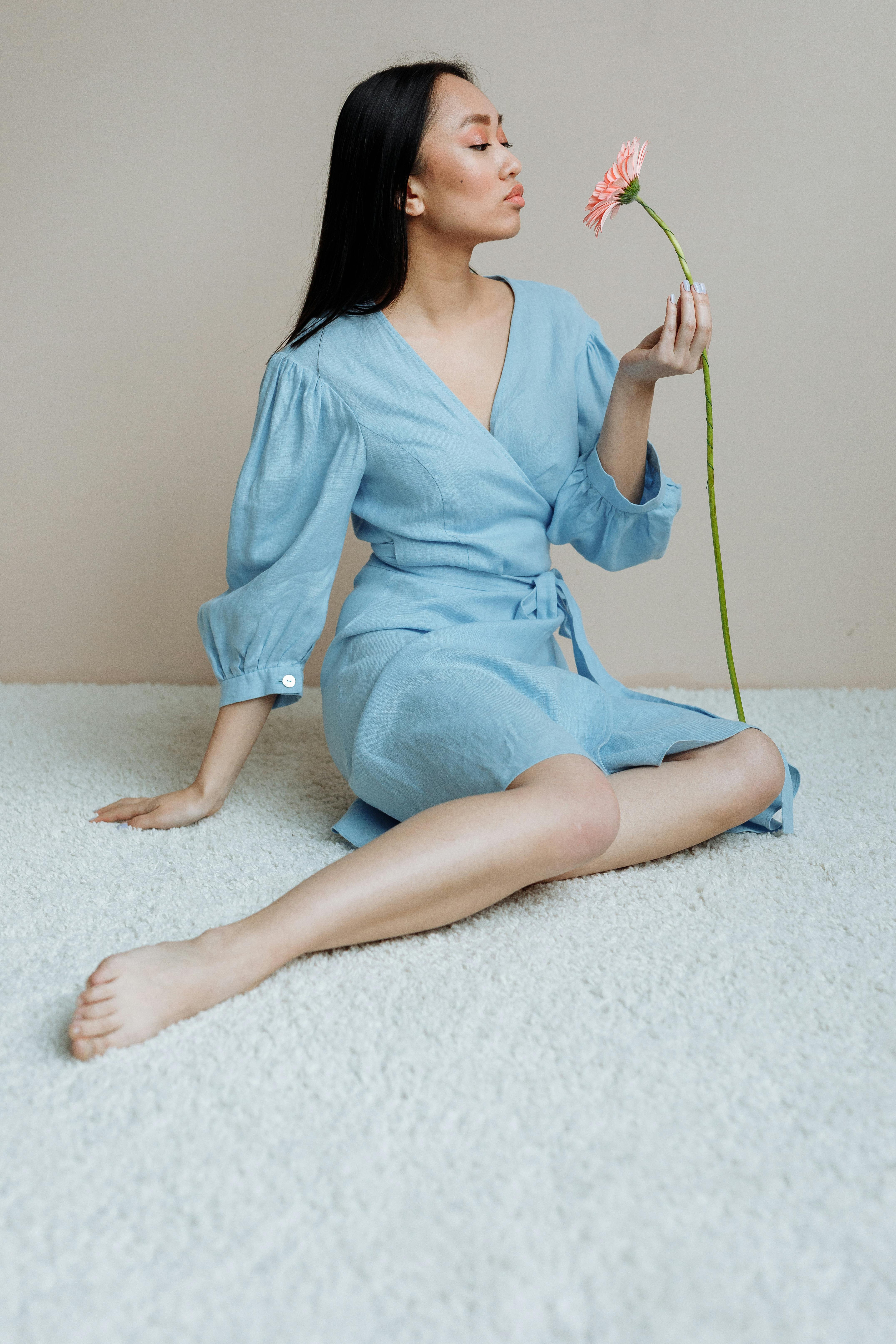 Woman in blue dress sitting gracefully holding a flower, exuding elegance.