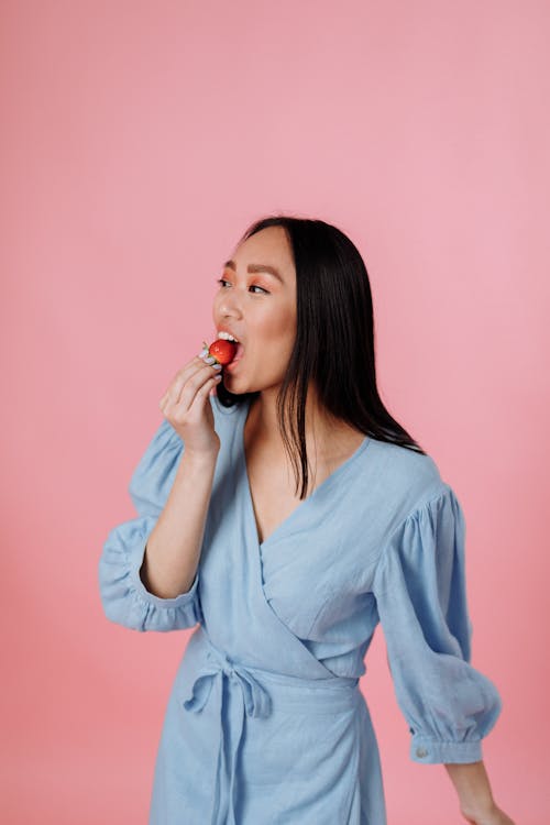 Woman in Light Blue Dress Eating a Strawberry