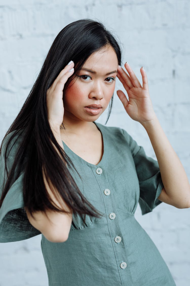 Woman In Blue Button Down Dress Holding The Temple Of Her Head While Seriously Looking At The Camera