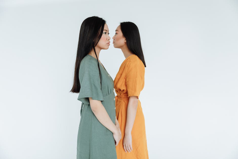 Two women stand face-to-face in colorful dresses against a white studio background.