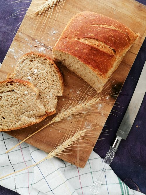 Free Sliced whole wheat bread on a wooden board with wheat stalks and a knife, perfect for baking and food photography. Stock Photo