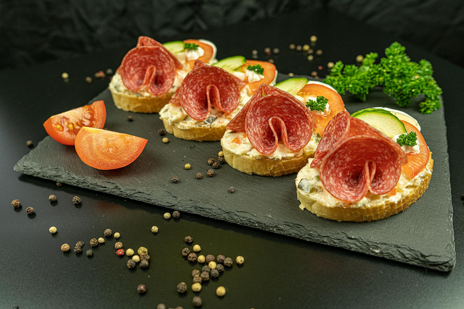 Tasty salami bruschetta served on a slate board with fresh vegetables and herbs.