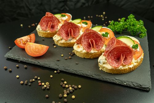 Free Tasty salami bruschetta served on a slate board with fresh vegetables and herbs. Stock Photo