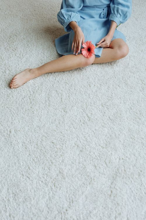 Free Stylish woman in blue dress sitting on a carpet holding a pink flower. Stock Photo