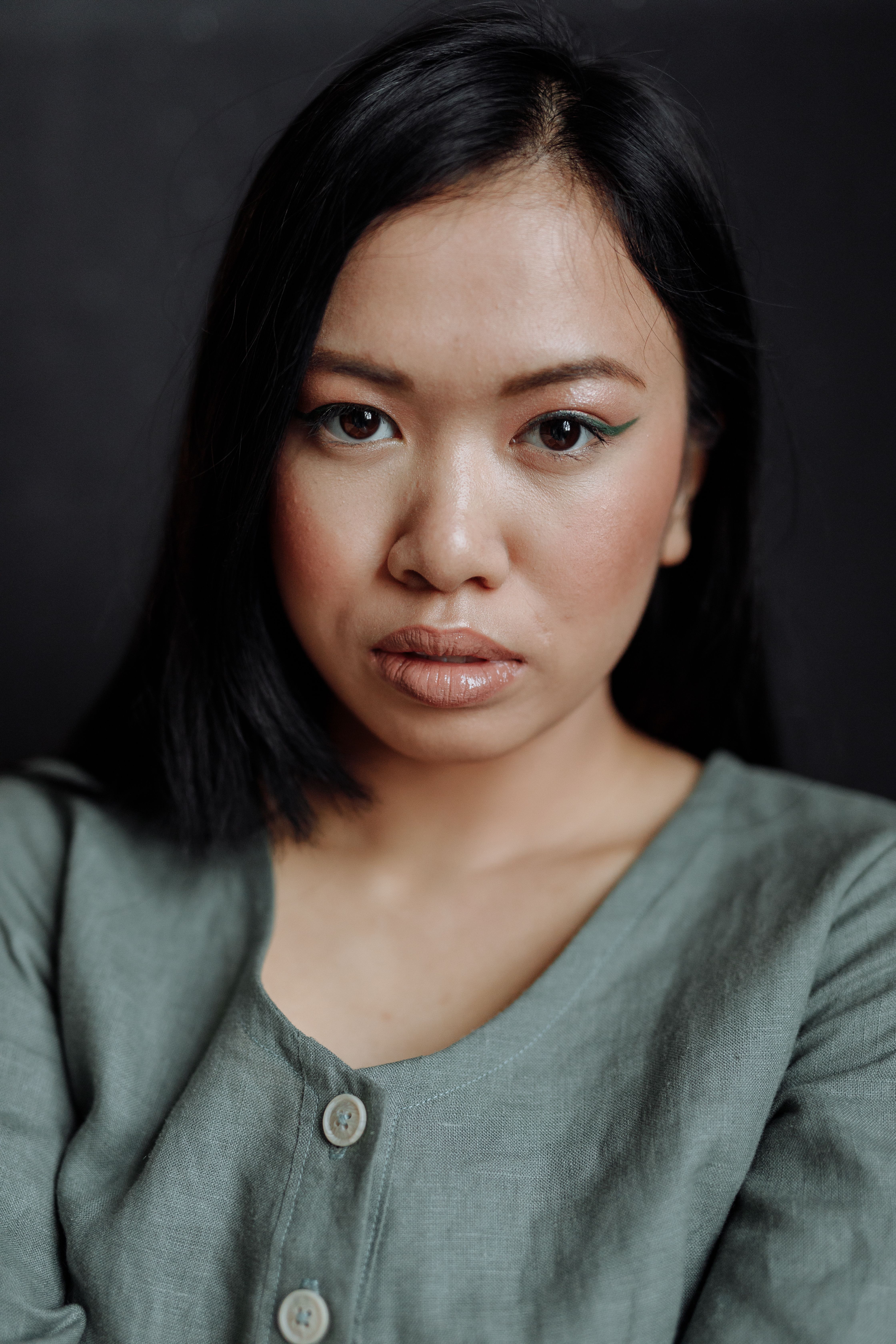 Close-up portrait of an Asian woman in a gray shirt, exuding a thoughtful and poised expression.
