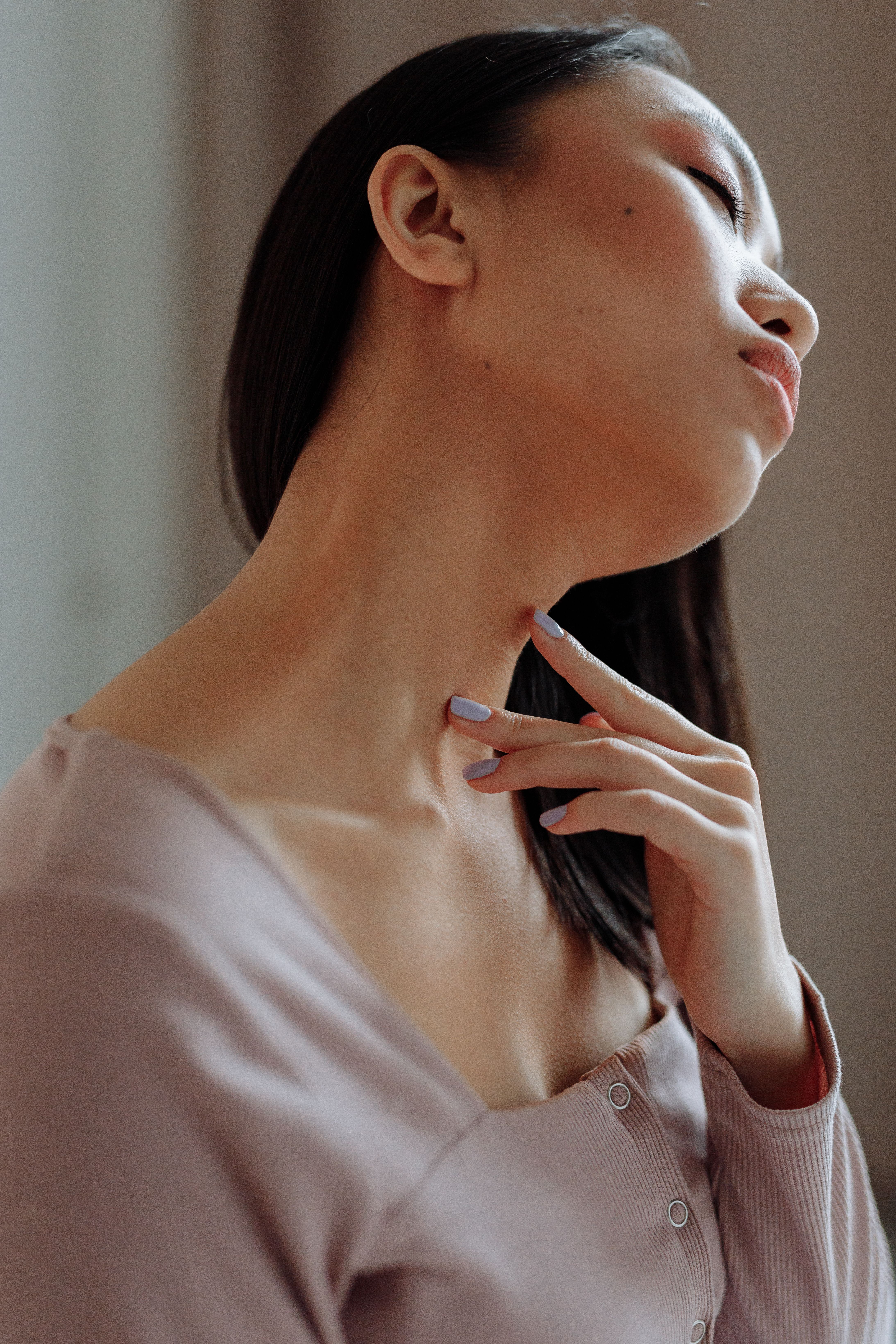 Close-up portrait of a woman with eyes closed, touching neck, in a purple sweater.