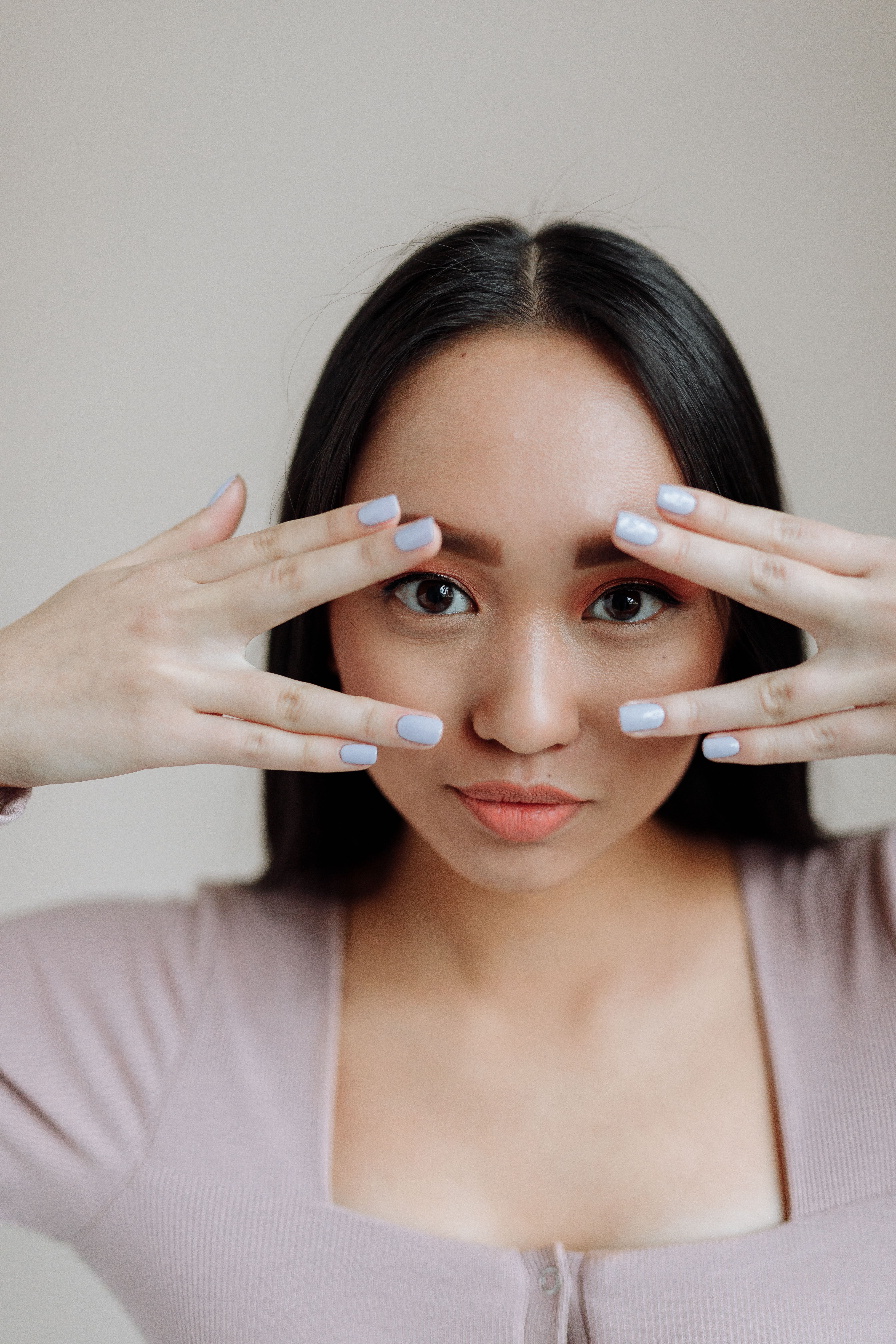 Close-up portrait of a young Asian woman framing her face with her hands, showcasing elegant simplicity.