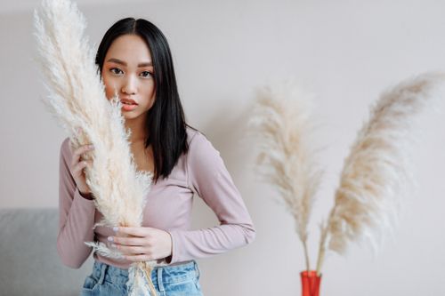 Free Stylish young woman posing indoors with pampas grass, creating a modern and natural look. Stock Photo