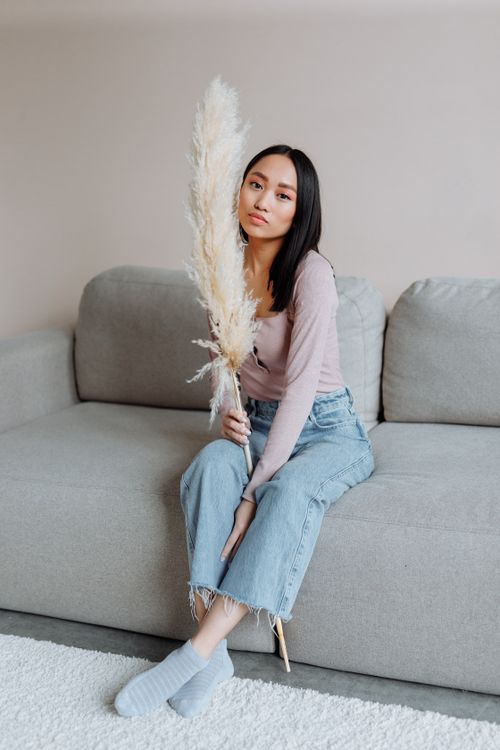 Free Elegant portrait of a woman holding pampas grass while sitting casually on a modern sofa. Stock Photo