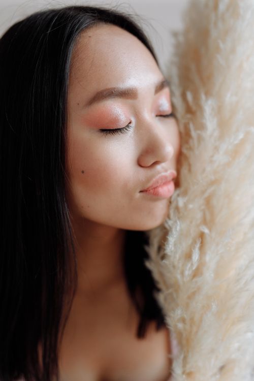 Free Close-up of an Asian woman with closed eyes gently touching pampas grass, exuding calmness. Stock Photo