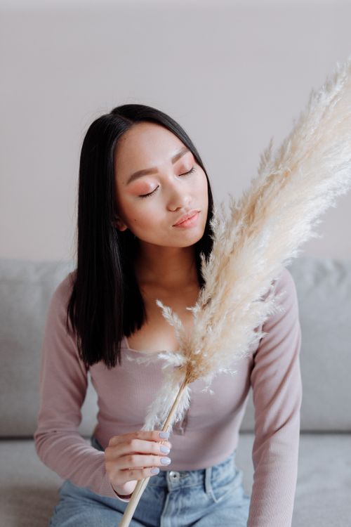 Free A serene portrait of a woman sitting with closed eyes, holding pampas grass indoors. Stock Photo