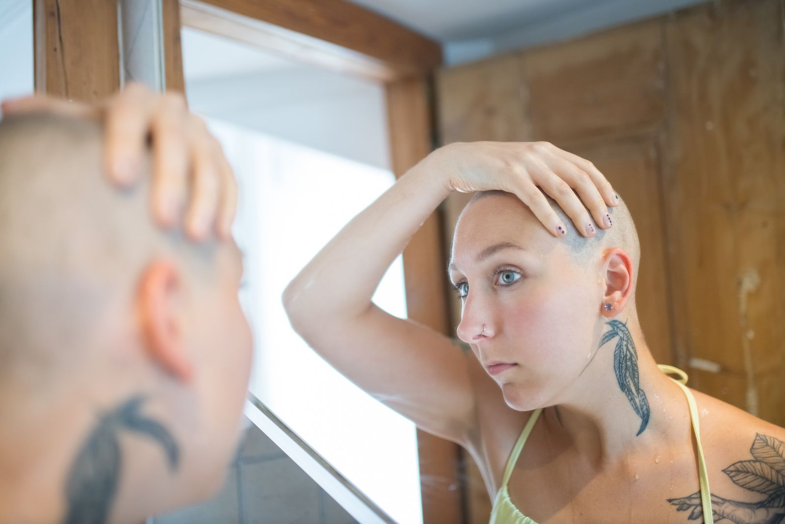 Woman with a bald head looking at her reflection in a mirror