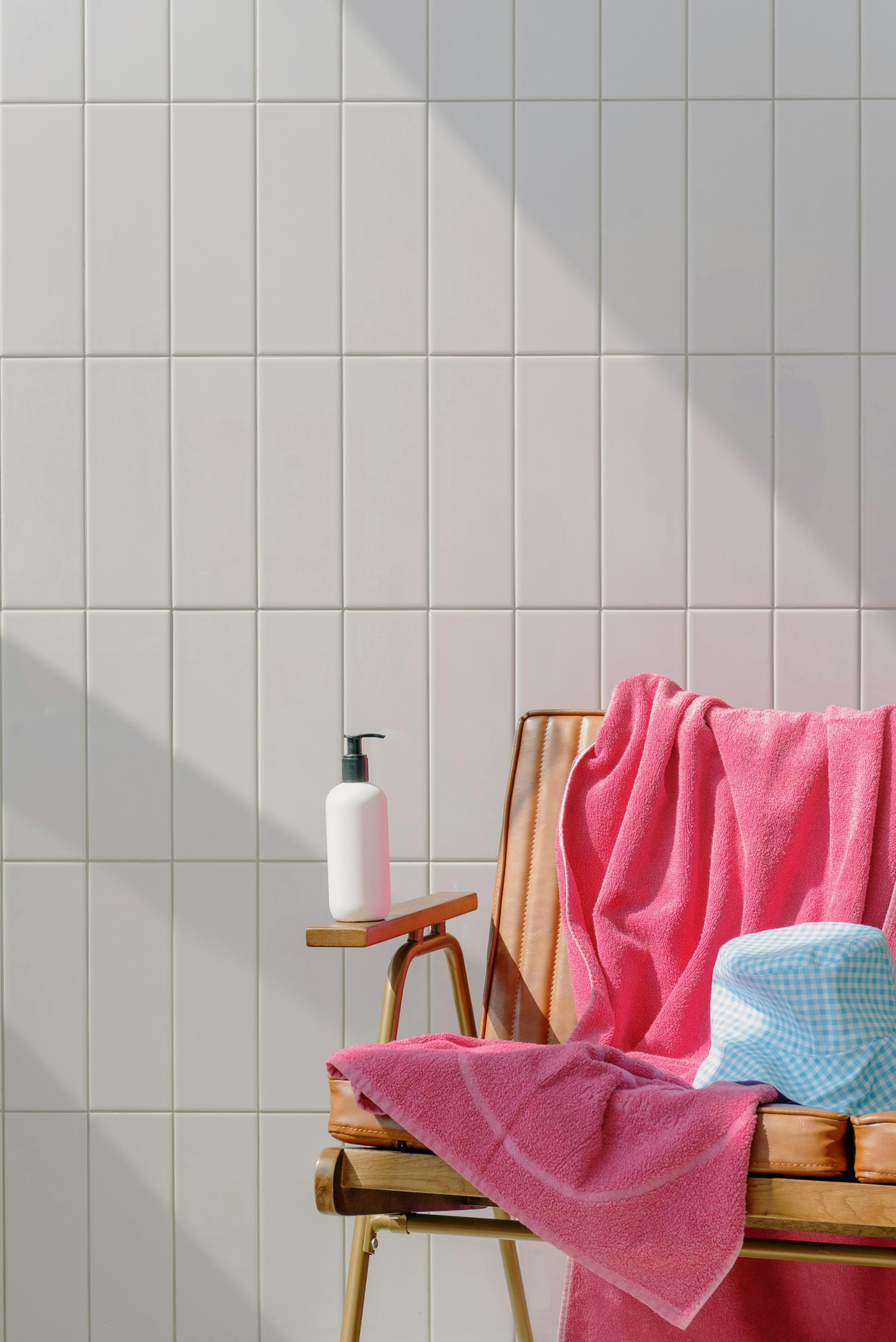 A calm poolside scene with a pink towel, lotion bottle, and hat on a chair.