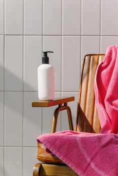 A modern bathroom setting with a lotion bottle on a wooden chair and a pink towel.