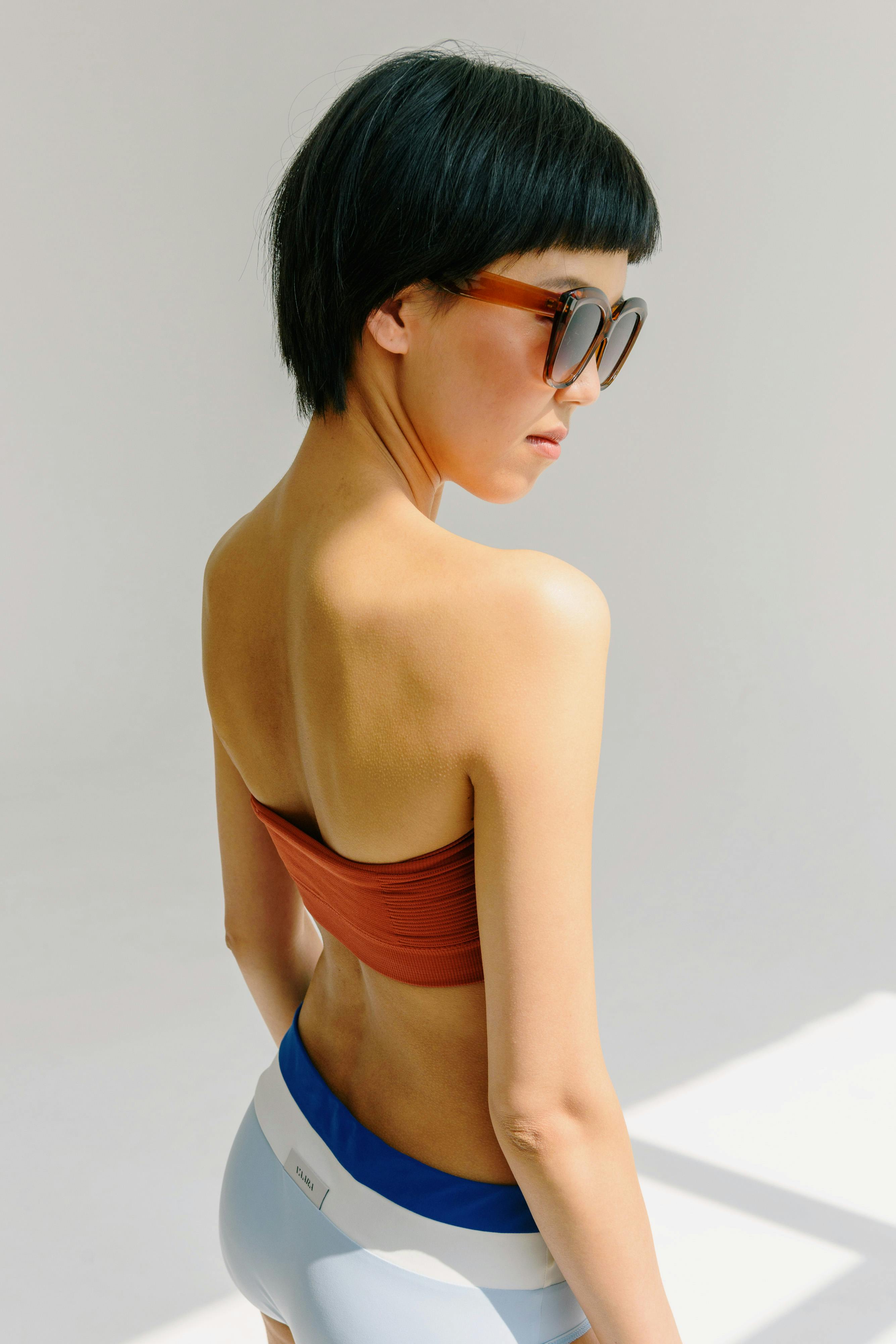 Contemporary portrait of a woman wearing sunglasses and a swimsuit in a studio setting.