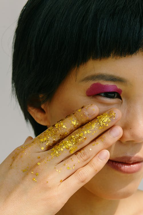 Model Touching Her Face with a Hand Covered in Golden Glitter