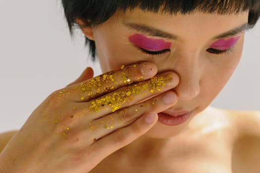 Close-up of a woman with pink eye shadow and gold glitter on her hand, enhancing beauty art.