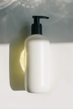 Close-up of a white skincare lotion bottle with pump in sunlight, ideal for branding.